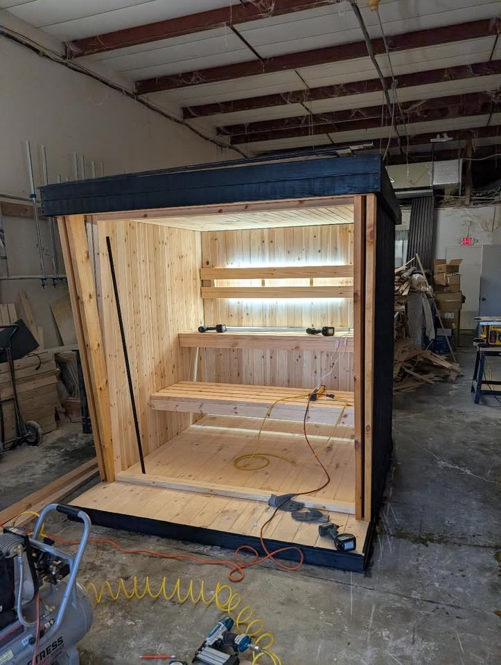 A sauna part-built on the workshop floor, tools and offcuts around it